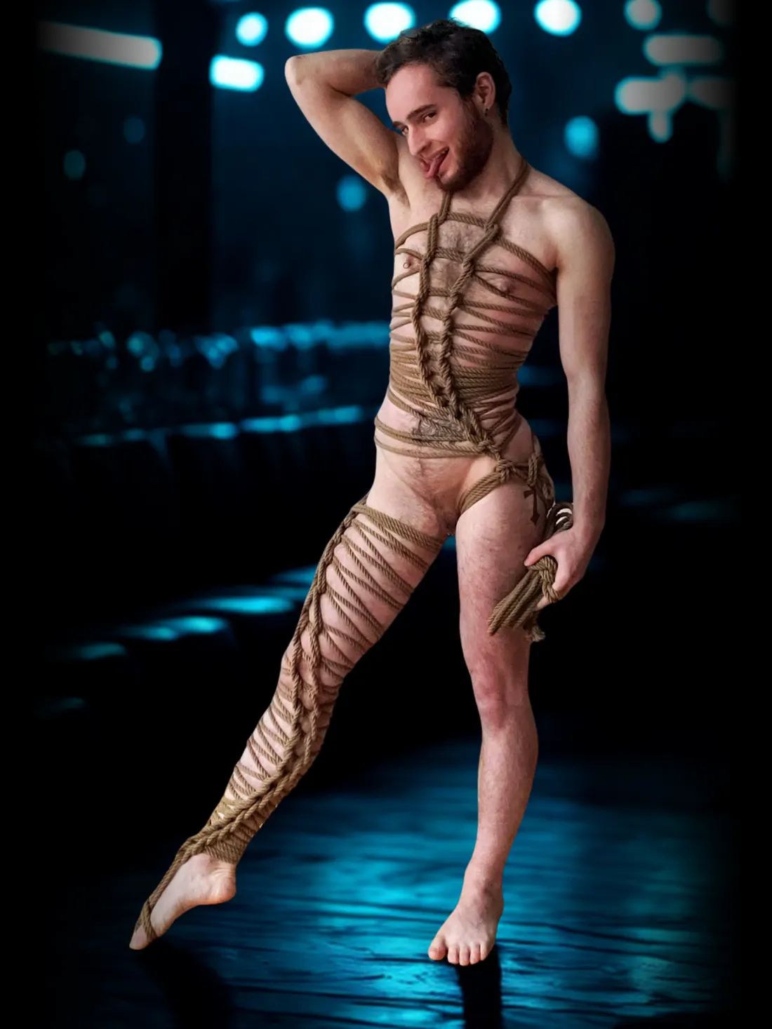 A dude wrapped head-to-toe in rope bondage, posing playfully on the dungeon floor under blue lights